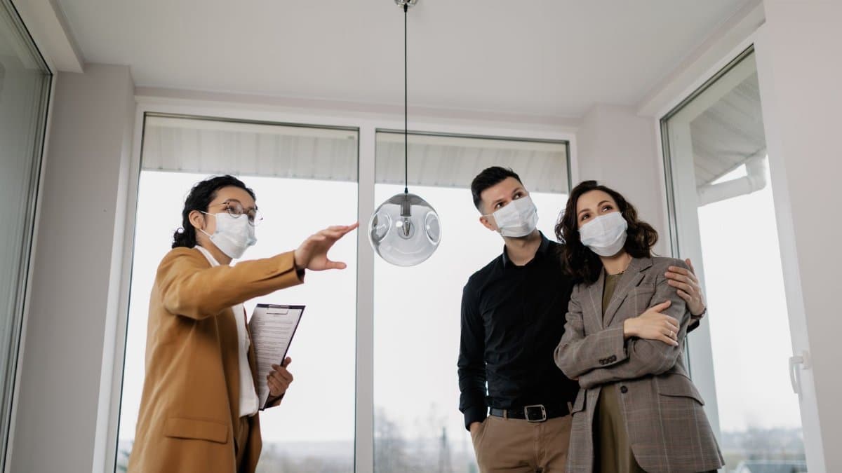 A realtor shows a masked couple a house interior, emphasizing safety during pandemic.