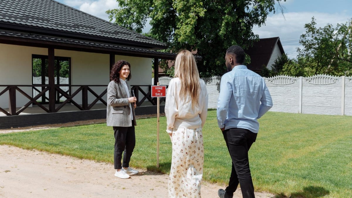 A diverse group viewing a house for sale with a real estate agent outdoors.
