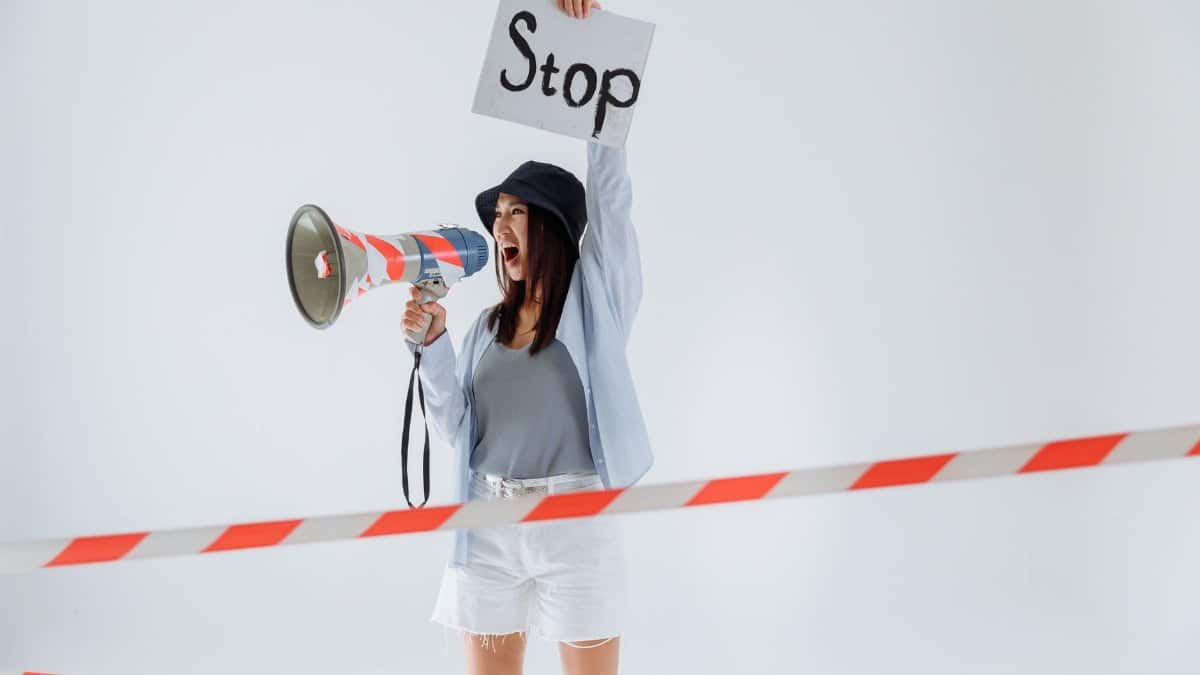 Woman holding a stop sign and megaphone while protesting in a studio setting.