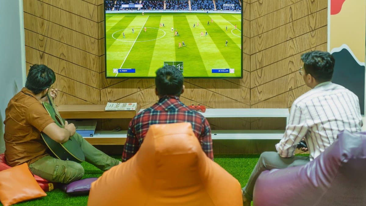 Three friends relaxing and playing a soccer video game indoors on a comfortable game night.