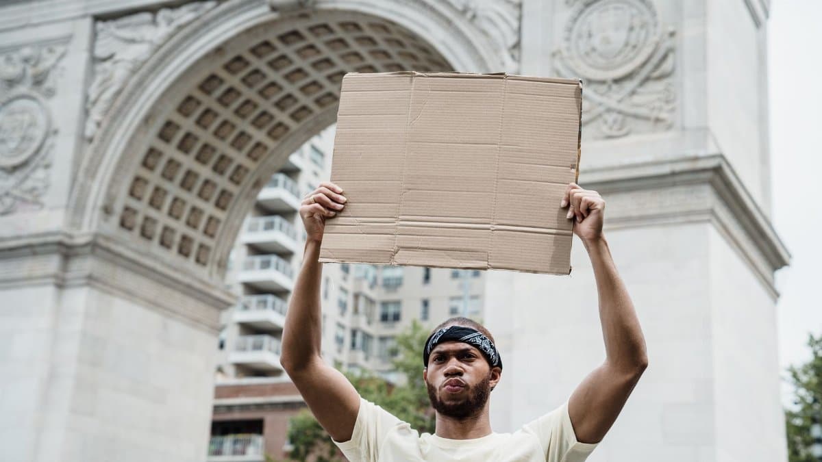 A man holds a blank cardboard sign near the Washington Square Arch, symbolizing activism and protest.