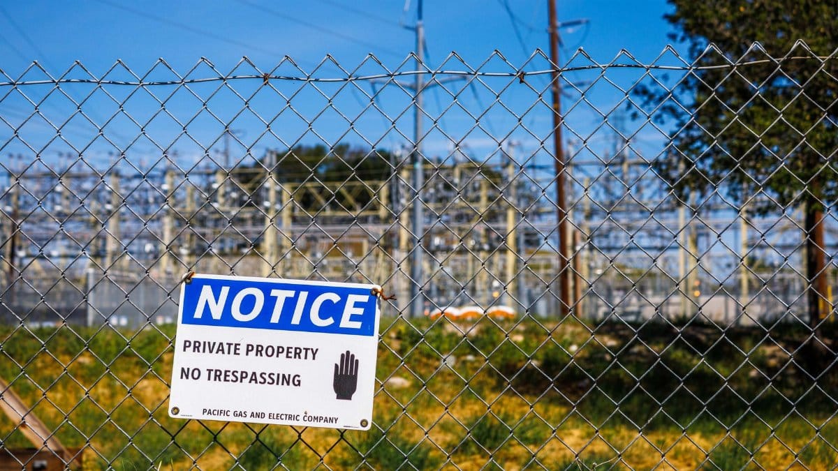 Chain link fence with a private property no trespassing notice sign and electrical infrastructure in the background.