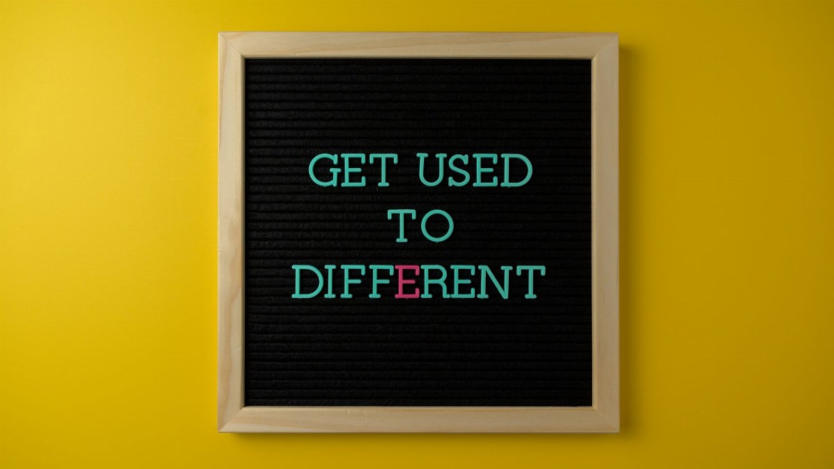 Letter board with 'Get Used To Different' message on vibrant yellow background.