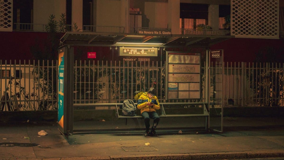 A person sitting alone at an illuminated bus stop in the city at night, creating a serene urban scene.