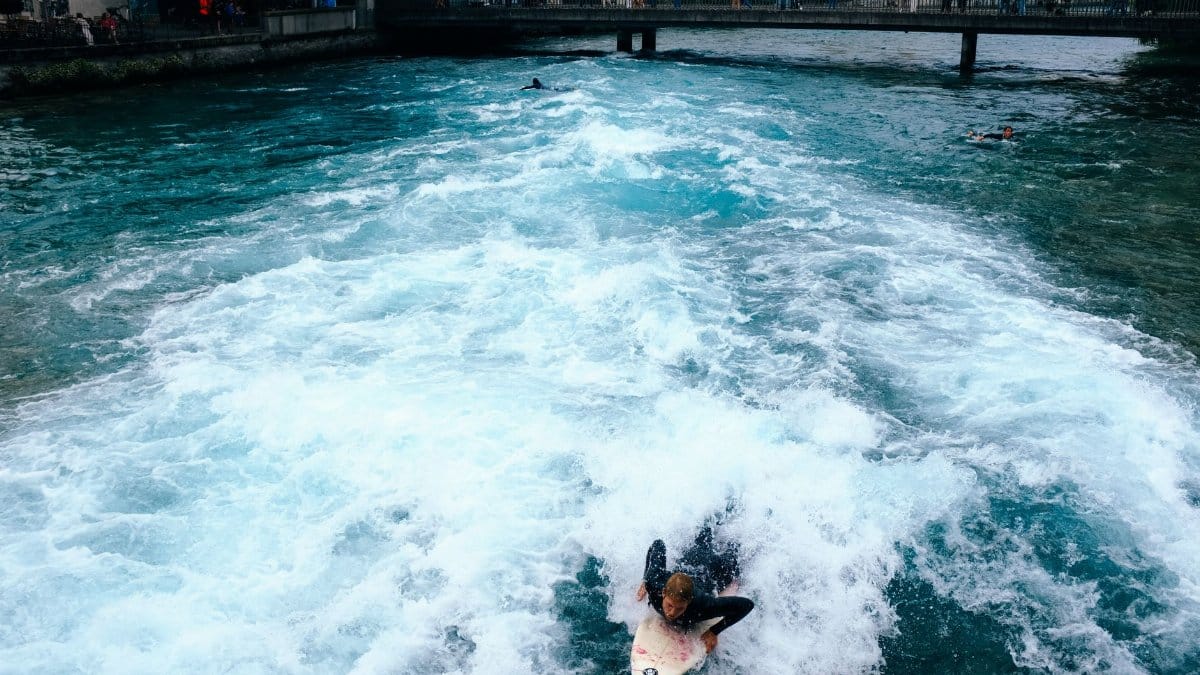 Surfer riding waves in a city canal, showcasing urban water sports and adventure.
