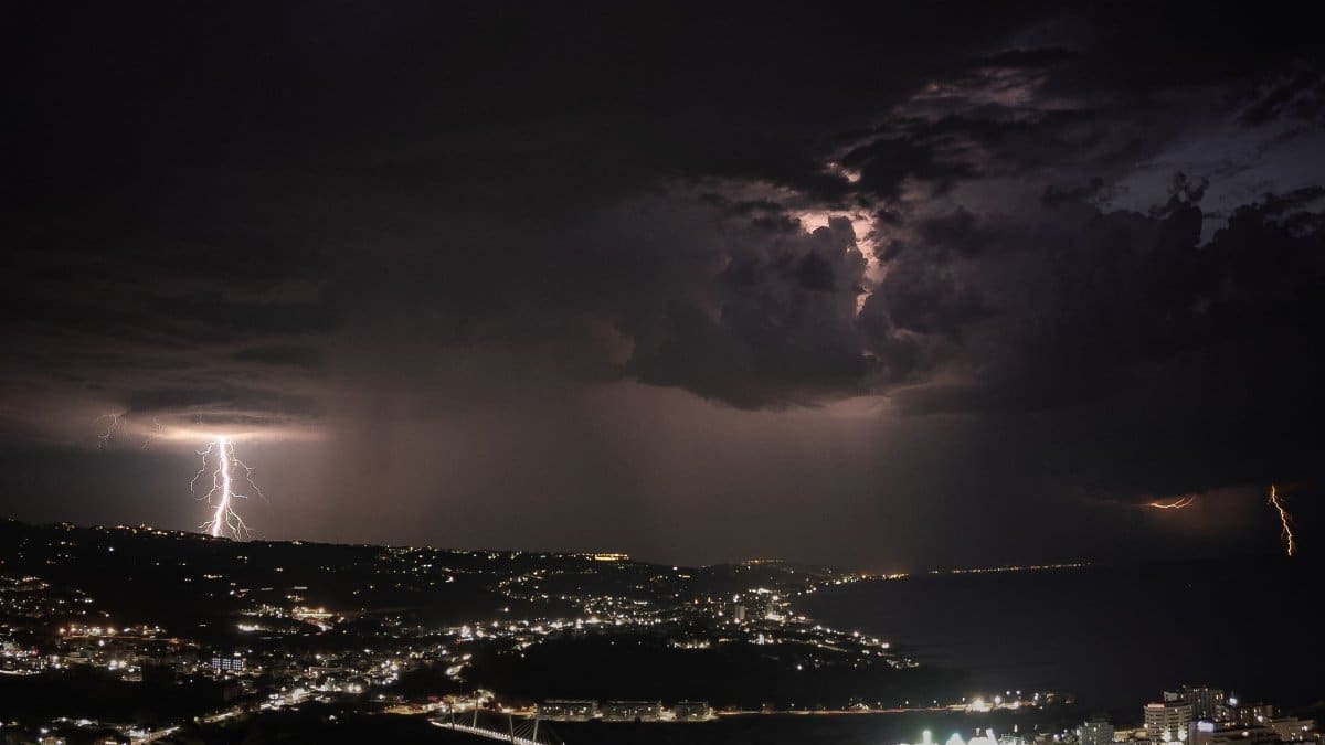 A striking night view of lightning storms illuminating a coastal city skyline.