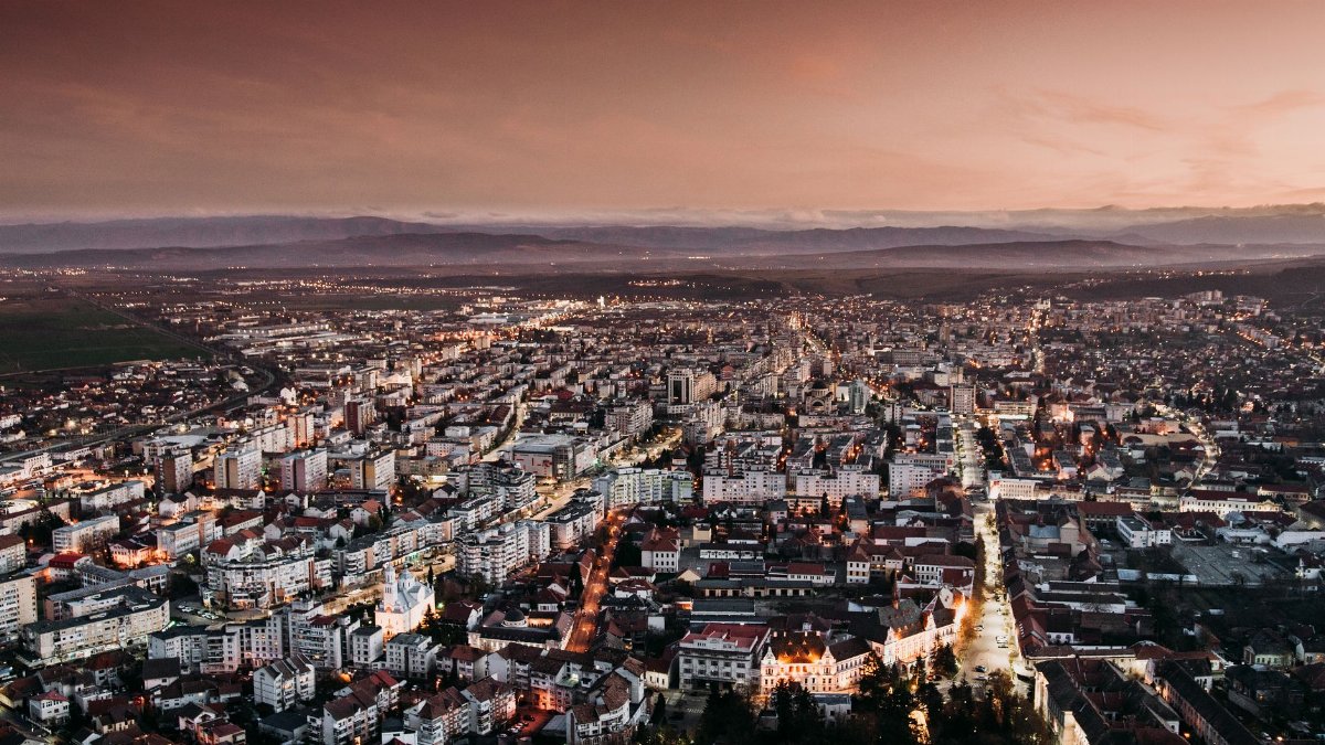 Stunning aerial view of Deva, Romania, captured at dusk with city lights illuminating the urban landscape.