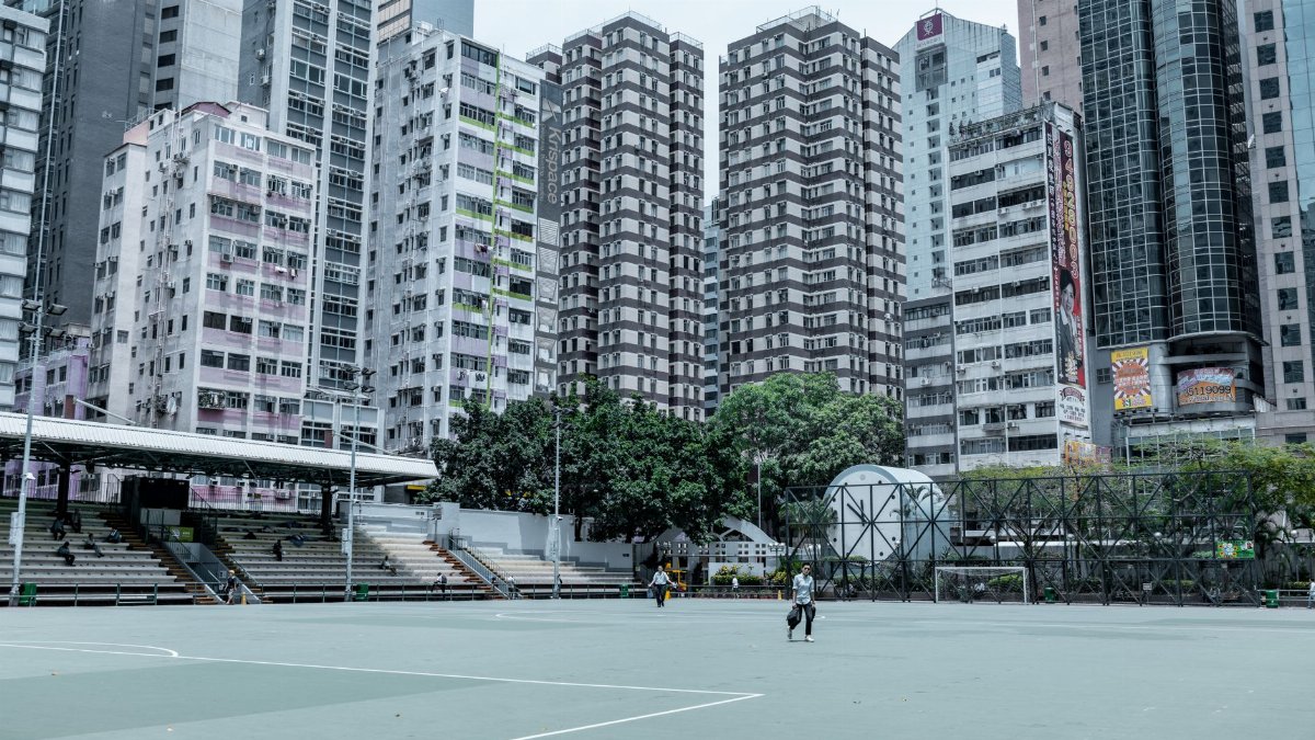 Wide shot of urban high-rise buildings with a sports field in the foreground, showcasing city life.