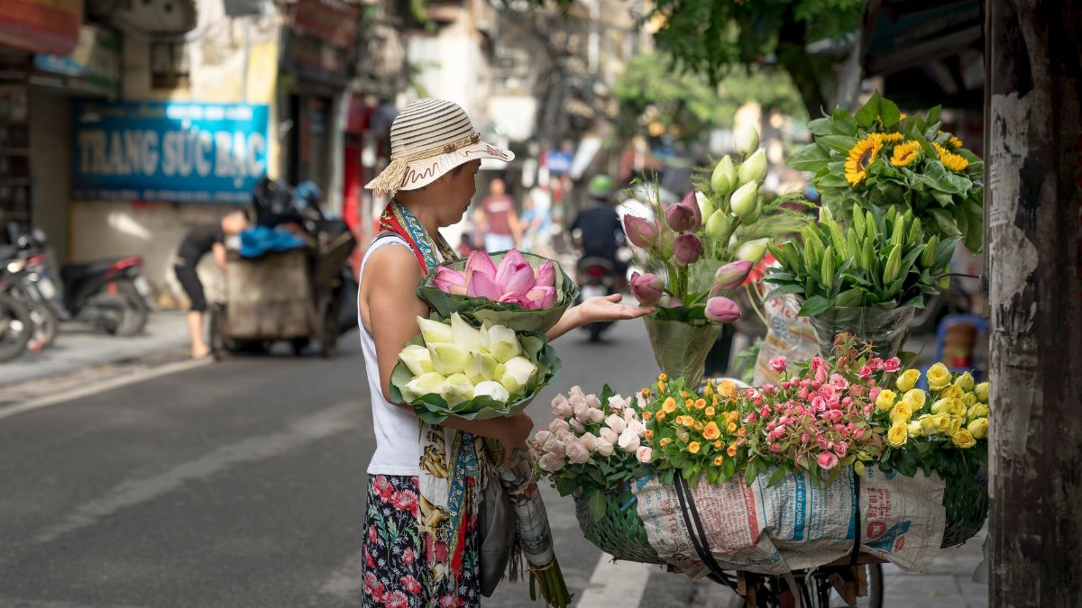 A street vendor sells vibrant bouquets from a bicycle in an urban setting.