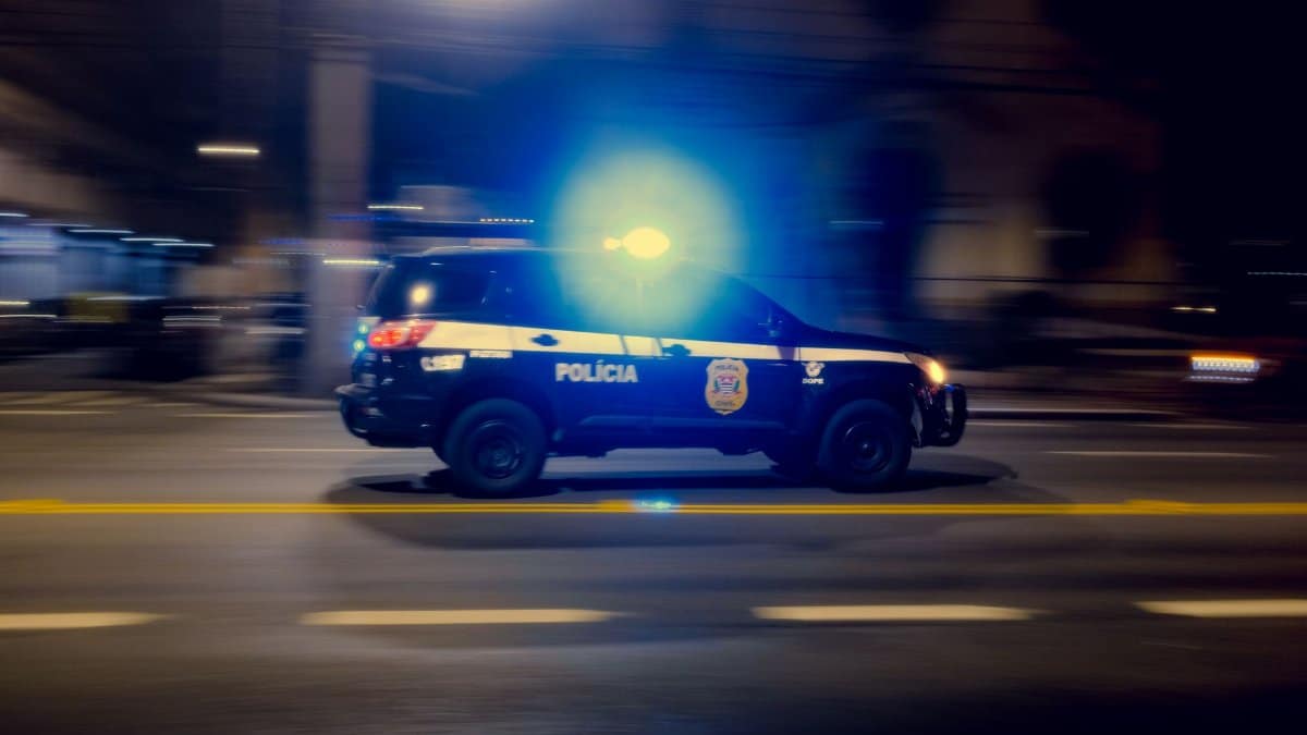 Blurred motion capture of a police car speeding at night with flashing lights on a city street.