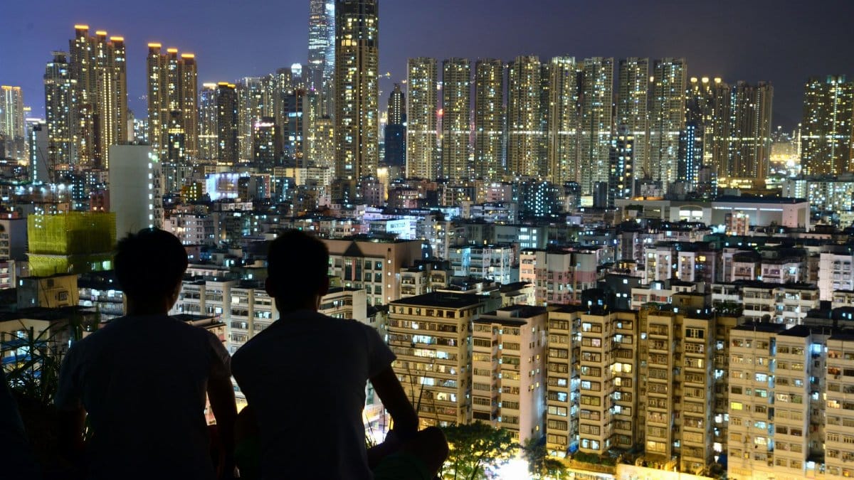 Two people silhouette overlooking illuminated city skyline at night, capturing urban beauty.
