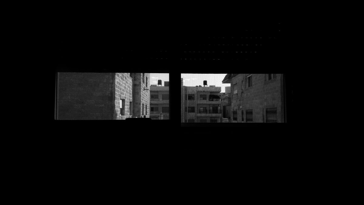 Black and white view of urban buildings through a window, highlighting city architecture.