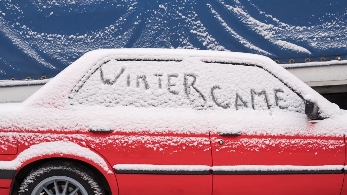 Snow-covered car with 'WINTER CAME' written on the window, showcasing a winter scene.