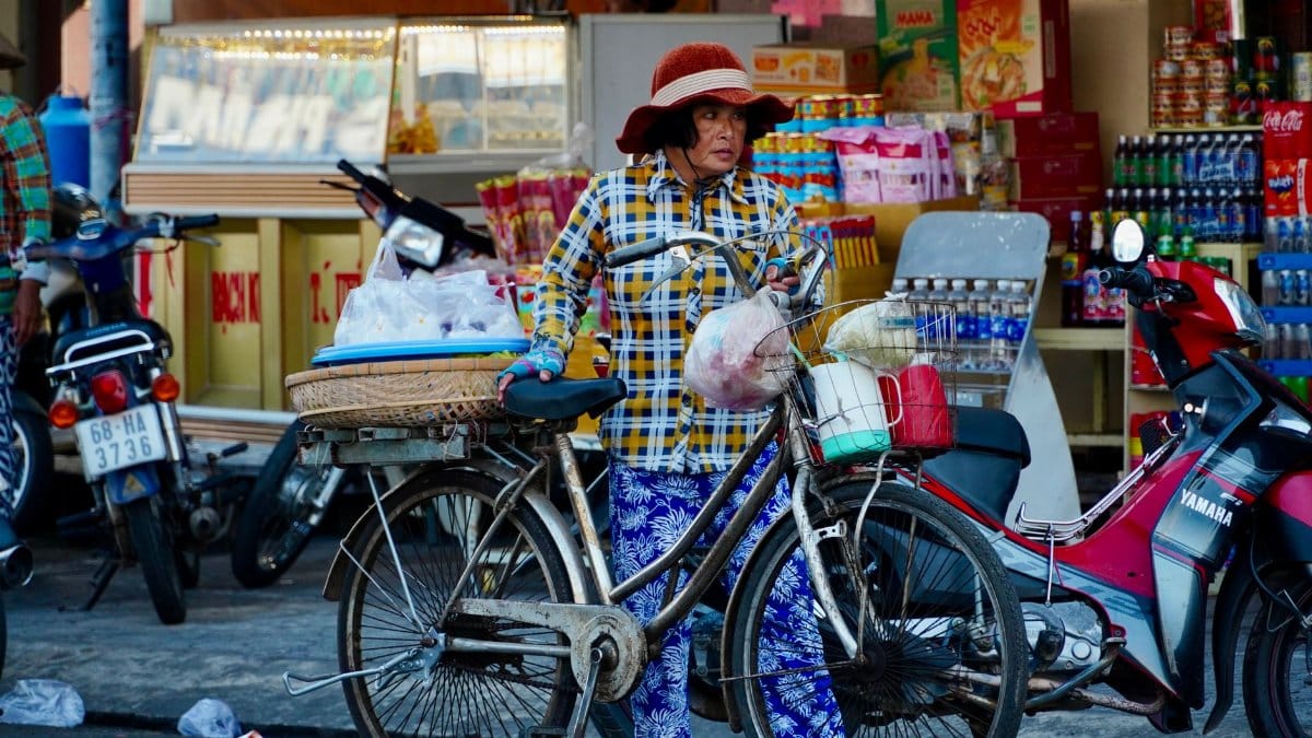 A woman street vendor with a bicycle in a vibrant market setting.