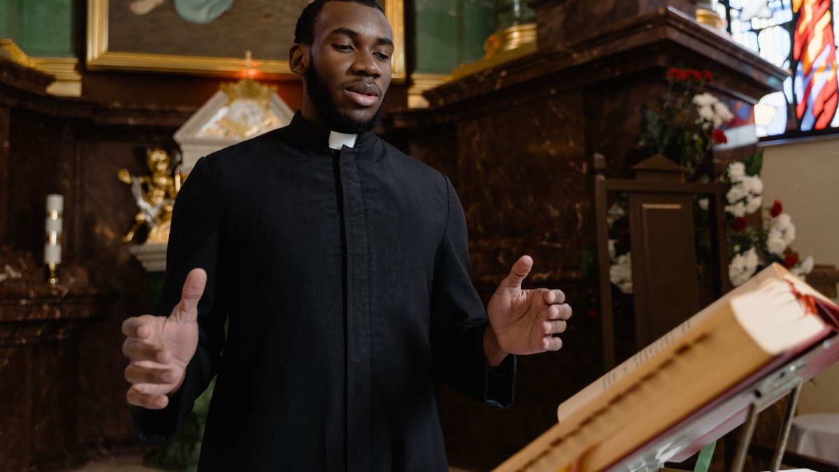 A priest delivering a sermon in a beautifully decorated church interior.