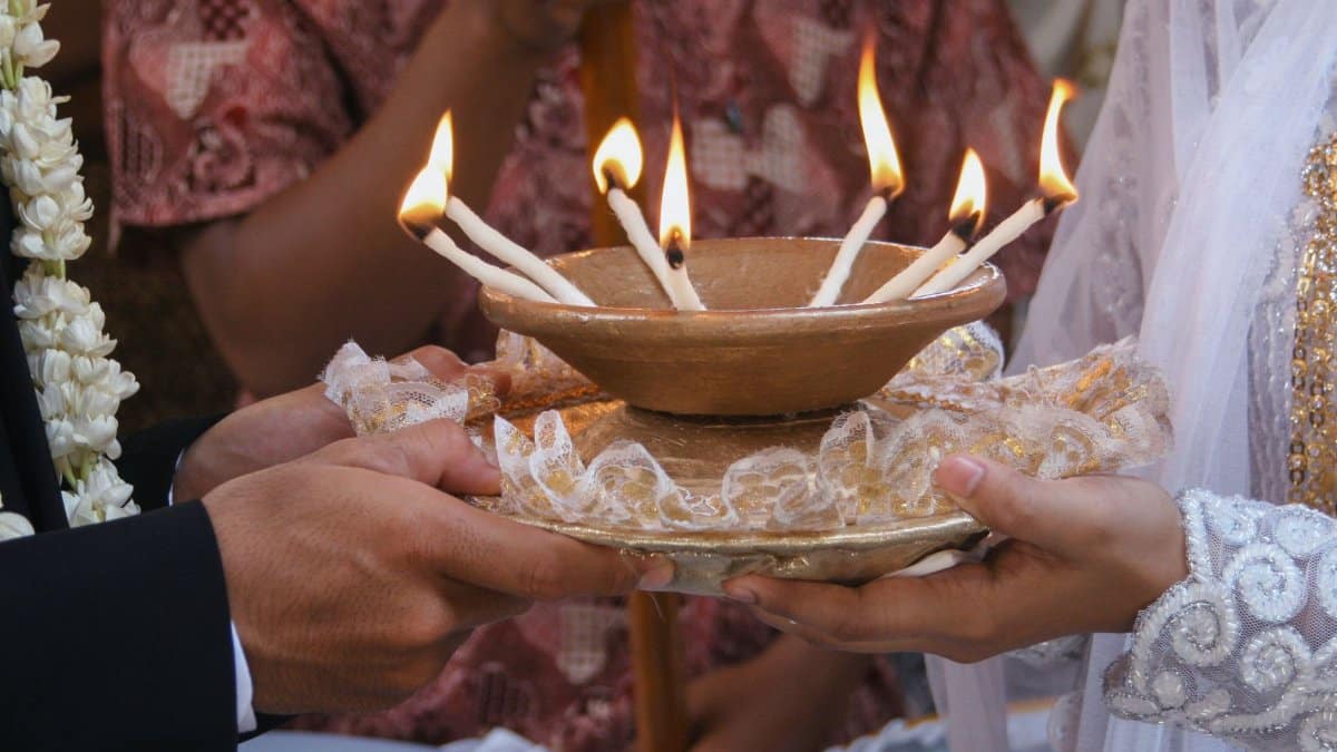 Close-up of a bride and groom holding a ceremonial bowl with candles during a wedding ritual.