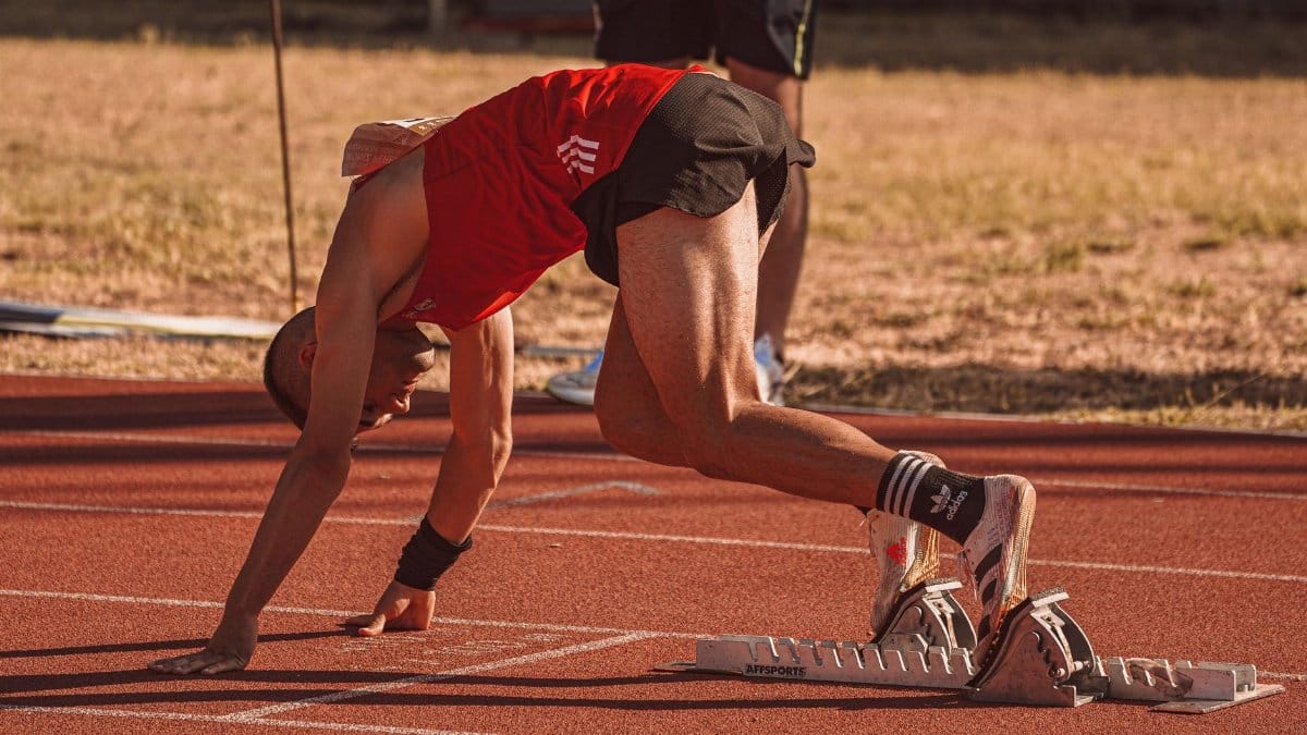 Athlete in red preparing to sprint on an outdoor track field. Focus on starting technique.