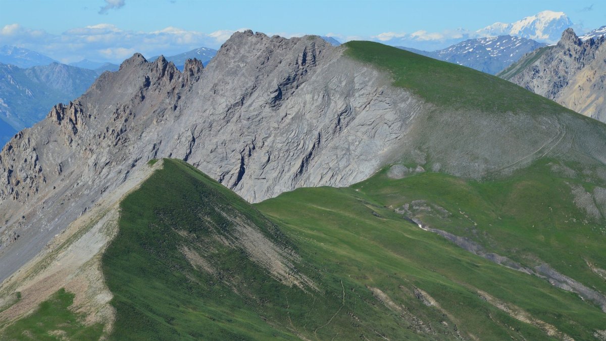 A breathtaking view of a mountainous landscape with green slopes and rocky peaks under a clear blue sky.