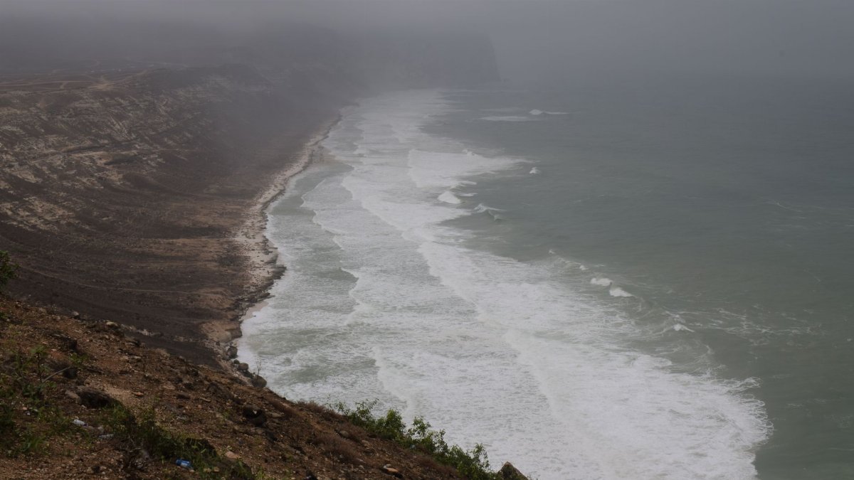 Dramatic view of a foggy coastline with waves crashing on the shore.