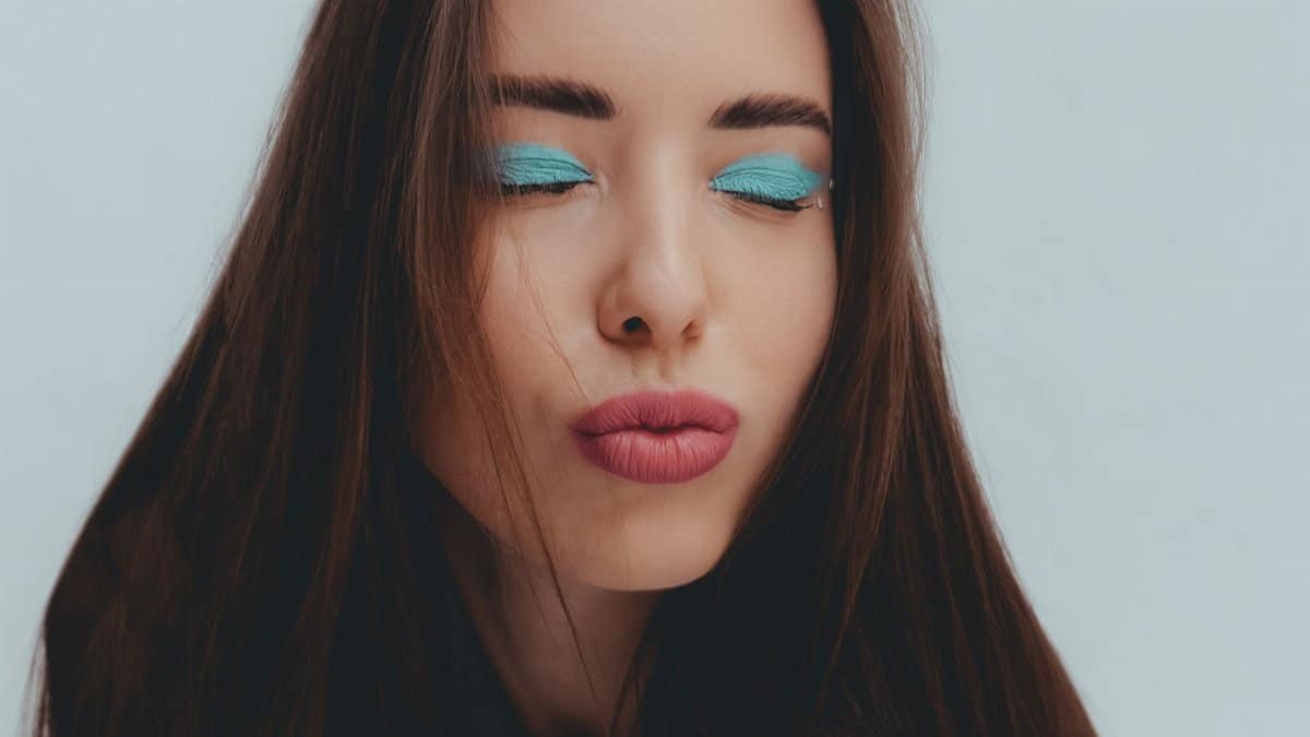 Studio portrait of a woman with vibrant blue eye shadow and pouting lips, eyes closed.