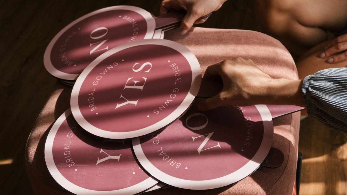 Close-up of hands holding pink bridal gown 'yes' and 'no' signs on a stool.
