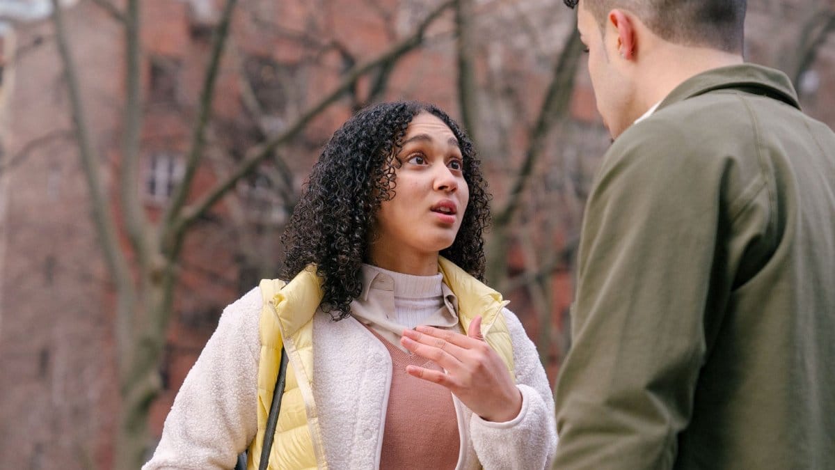 From below of ethnic female with short curly hair standing and arguing with boyfriend on street in daylight
