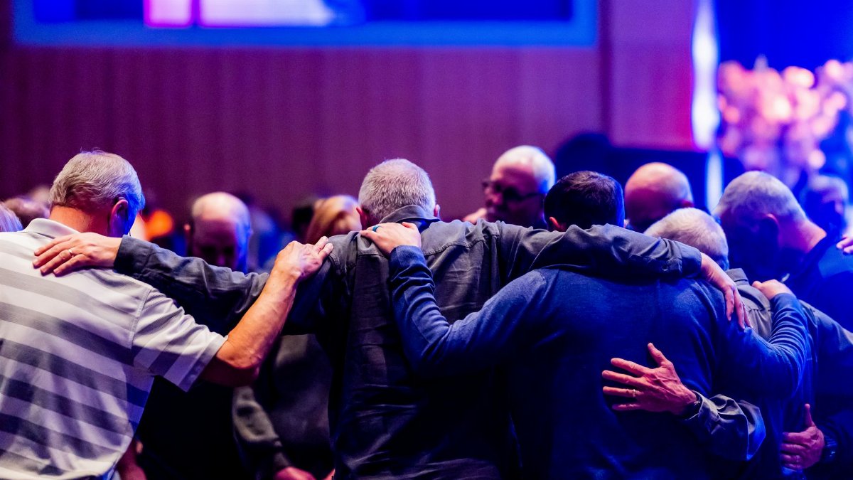A congregation of men embracing and praying together in a church setting.