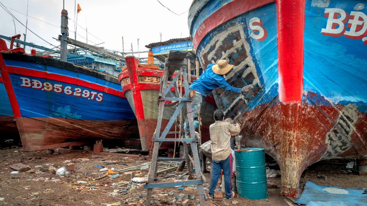 A group of men working together to repair fishing boats in a shipyard setting.