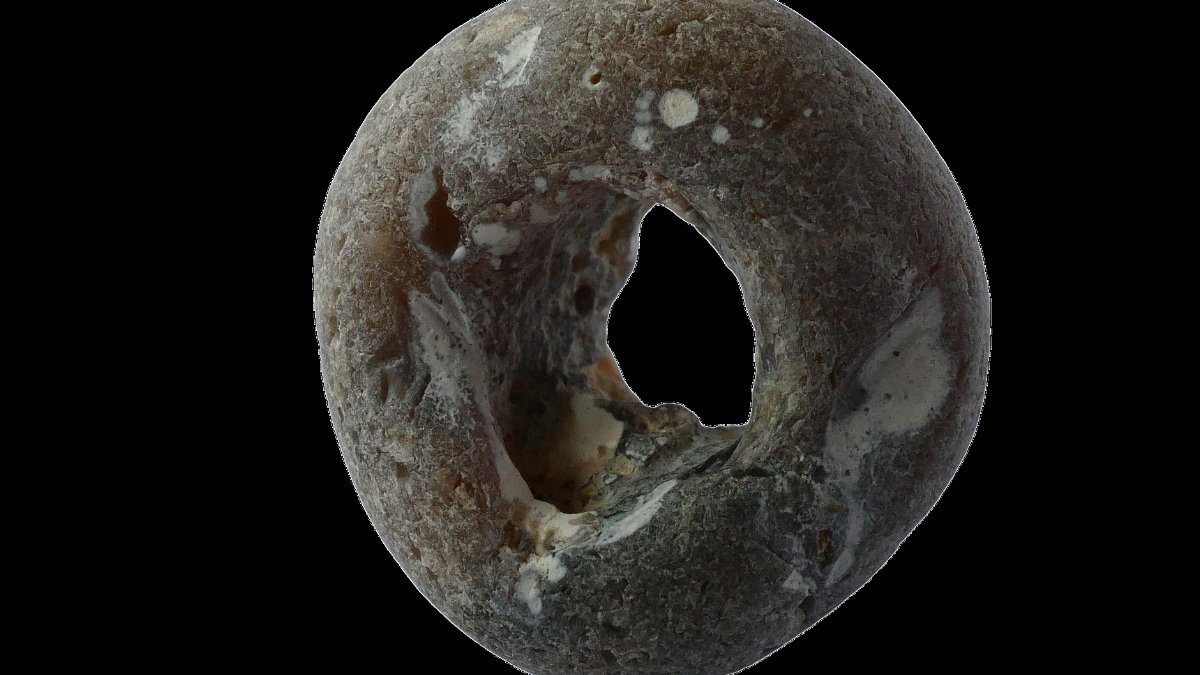 Close-up of a naturally weathered stone with a circular hole, resembling a donut shape.