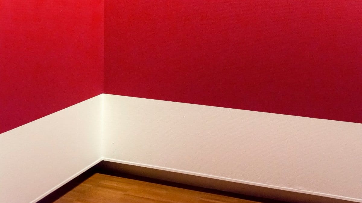 A minimalist room corner with striking red walls and wooden flooring, showcasing modern design.