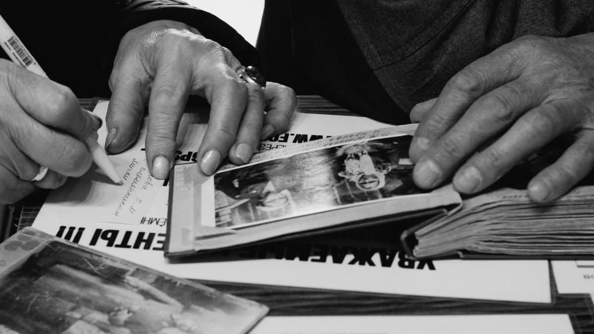 Hands of elderly people examining and writing in photo albums, capturing memories.