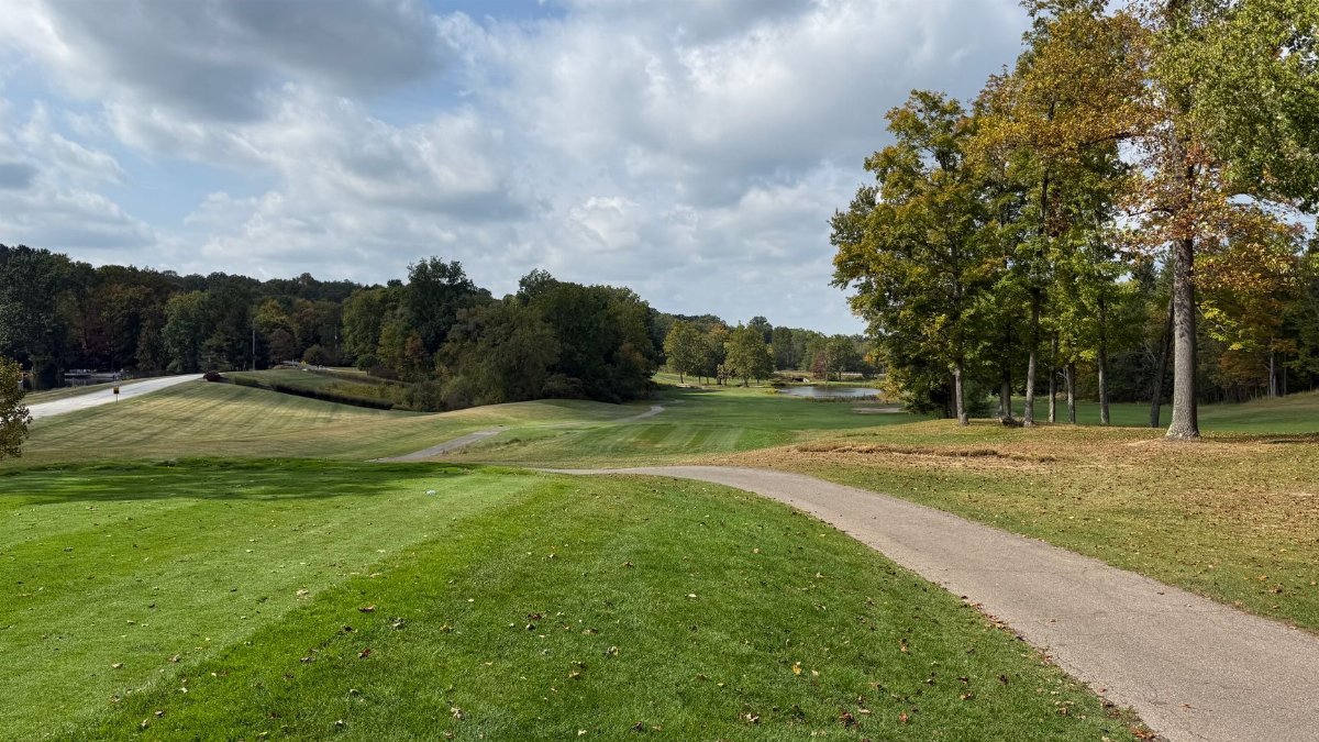 Beautiful golf course with lush greens and fall foliage under a partly cloudy sky.