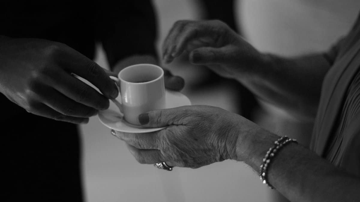 Close-up of hands exchanging a small coffee cup in a serene black and white setting.