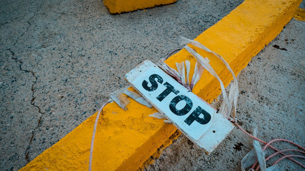 A worn 'STOP' sign placed on a cracked concrete pavement next to a yellow curb.