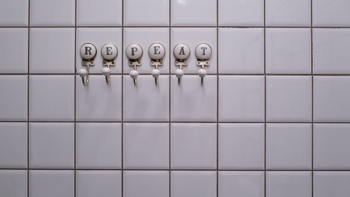 White tiled wall with towel hooks spelling 'REPEAT', showcasing a conceptual minimalist design.