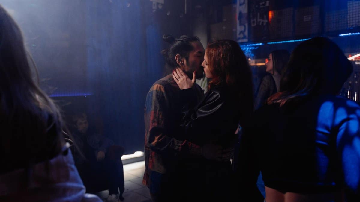 A romantic couple kissing in a lively nightclub with colorful lighting.