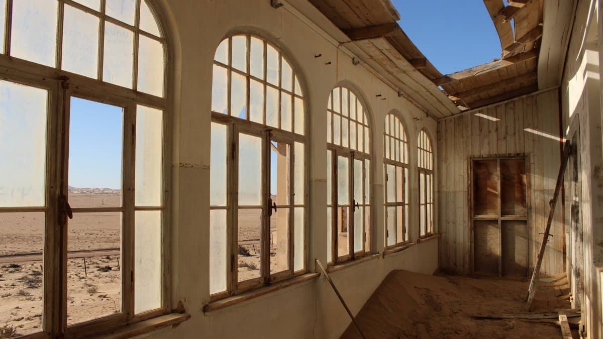 Interior of an abandoned building with arched windows illuminating a desert view and decayed structure.
