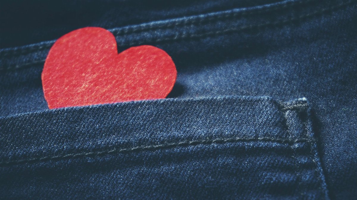 A red heart-shaped paper in a denim jeans pocket symbolizing love and Valentine's Day.
