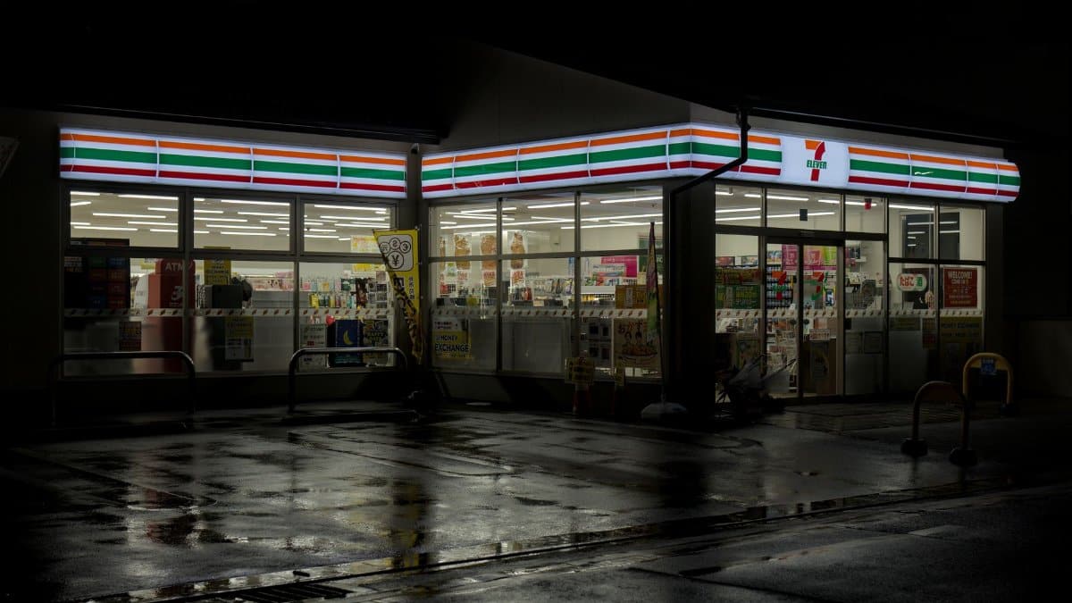 Illuminated 7-Eleven in Kyoto reflecting on wet street at night.