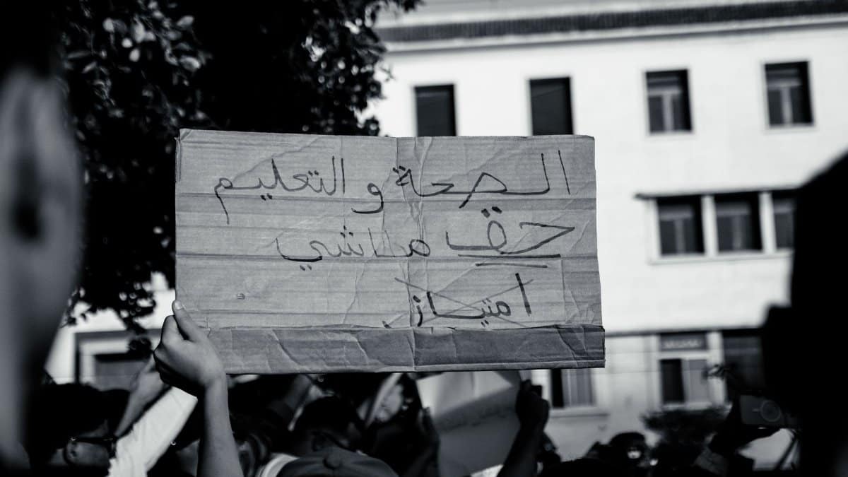 Black and white photo of a protest with people holding a sign, emphasizing social justice themes.