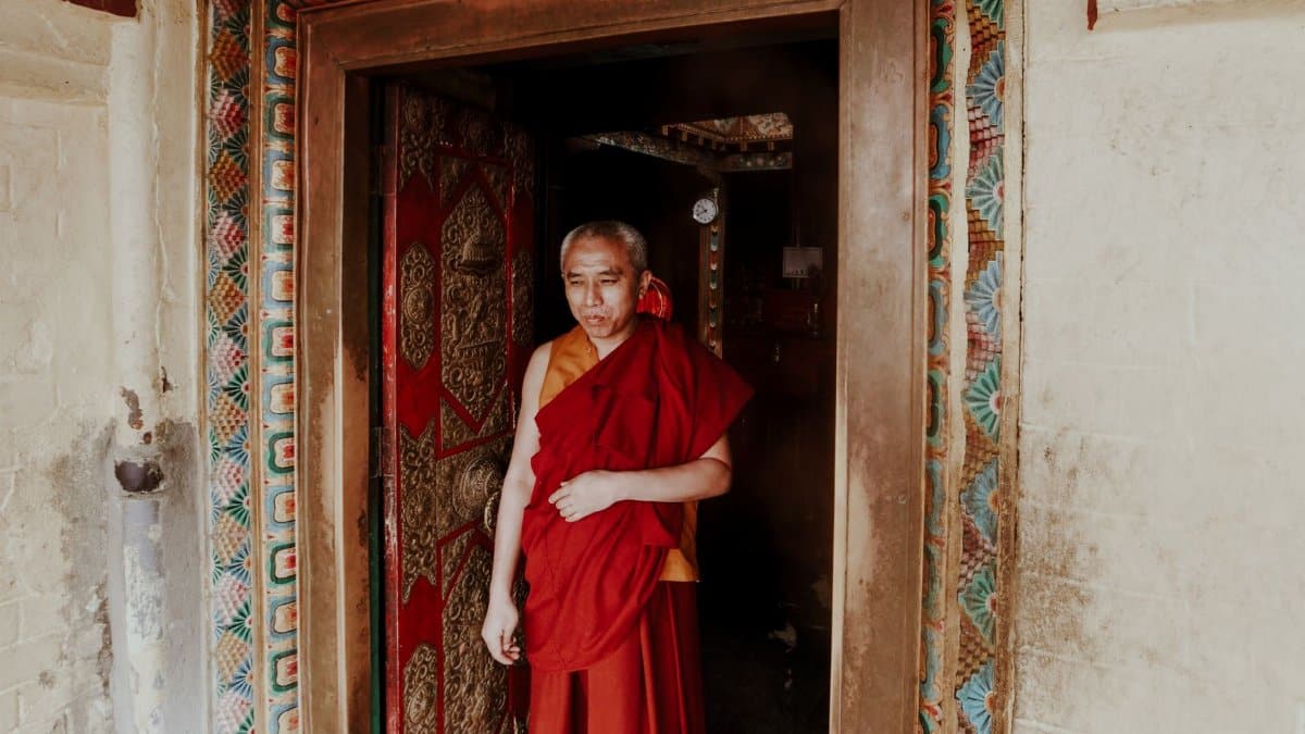 Elderly Buddhist monk standing in an ornate temple doorway, reflecting spirituality.