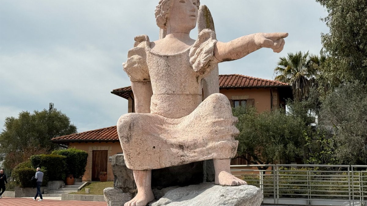 A grand stone statue depicting a seated figure pointing, set in a landscaped outdoor area.