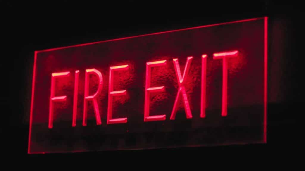 Brightly lit red neon fire exit sign illuminating in a dark setting.
