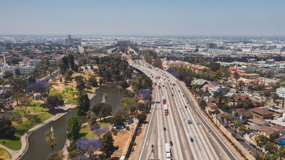 Aerial view of a busy Los Angeles freeway flanked by a verdant park and urban landscape.