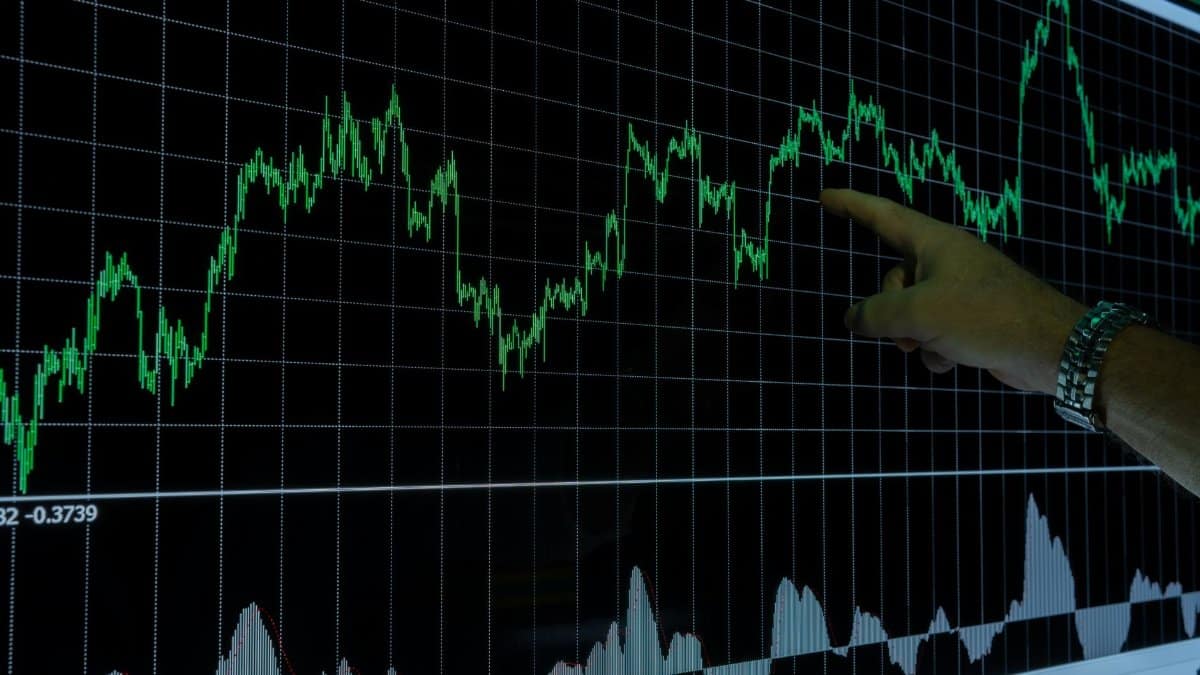A hand points to a financial graph on a digital screen, indicating market trends.