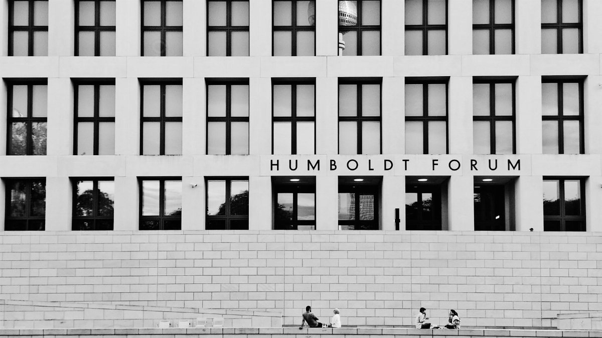 Black and white photo of Humboldt Forum's facade with a reflection of Berlin TV Tower and people sitting outside.