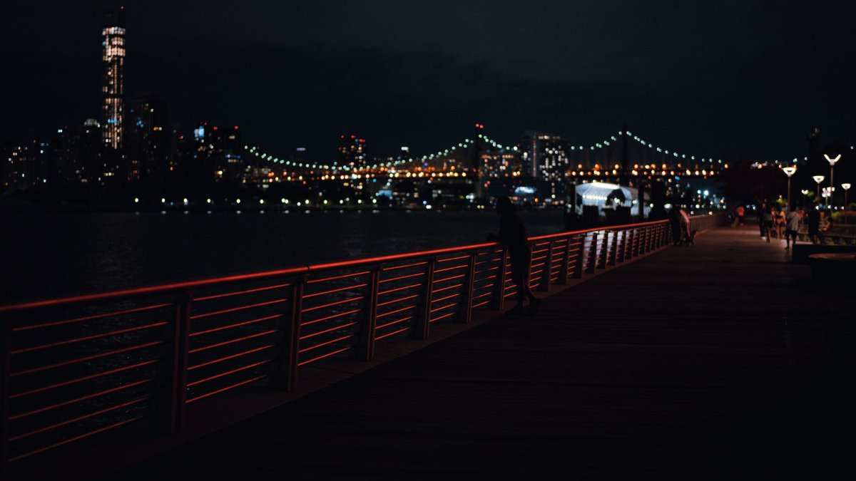 Beautiful city skyline and bridge illuminated at night with people walking on the boardwalk.