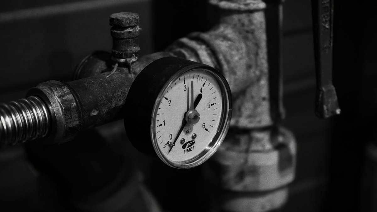 Close-up of a vintage pressure gauge on industrial pipes in monochrome.