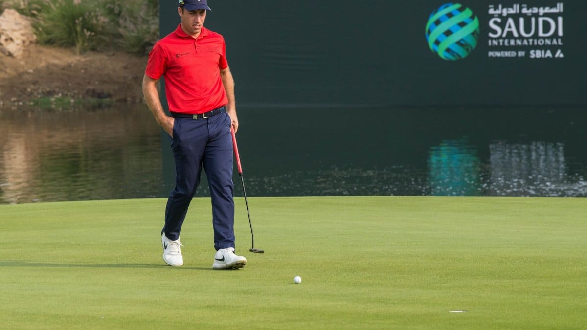 A male golfer in red shirt on a golf course at Saudi International event.