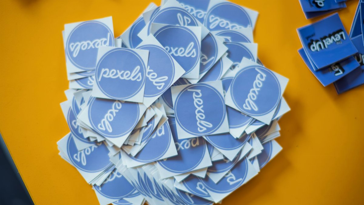 Pile of blue Pexels stickers on a vibrant yellow surface, top view.